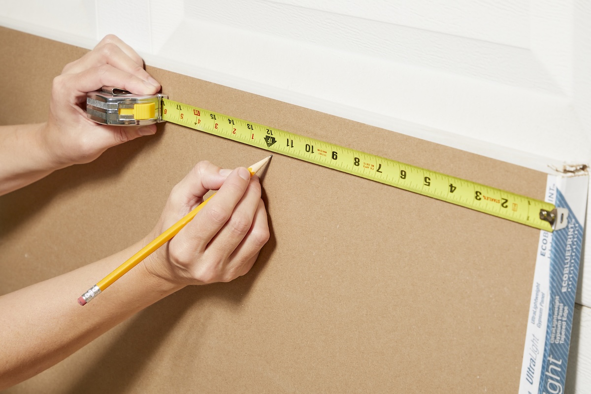 Hands marking a piece of drywall for cutting.