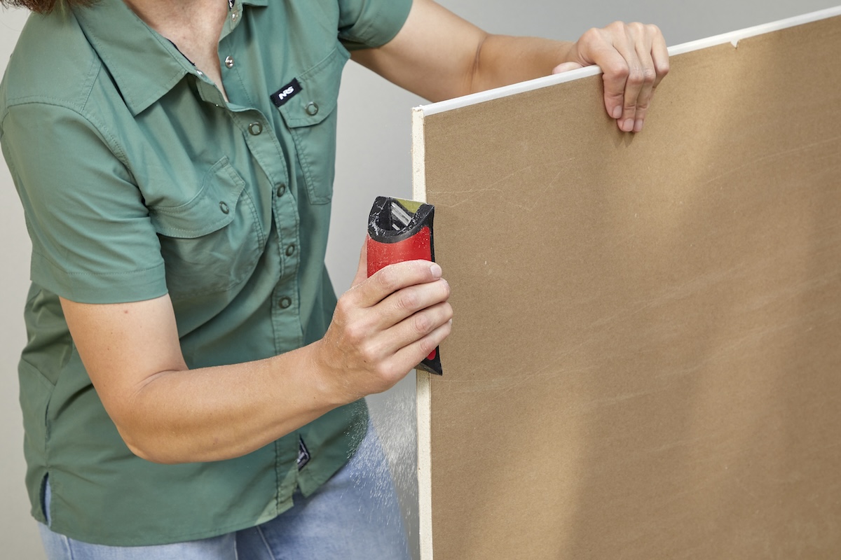 A person using a rasp to smooth the cut edge of a sheet of drywall.