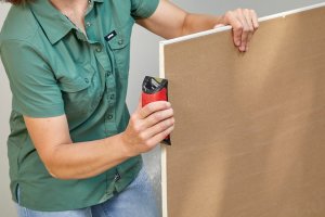 A person using a rasp to smooth the cut edge of a sheet of drywall.