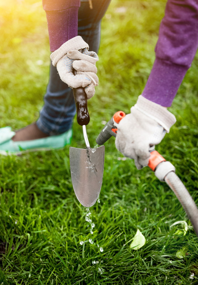 Closeup of woman wearing gloves and washing garden tools with hose.