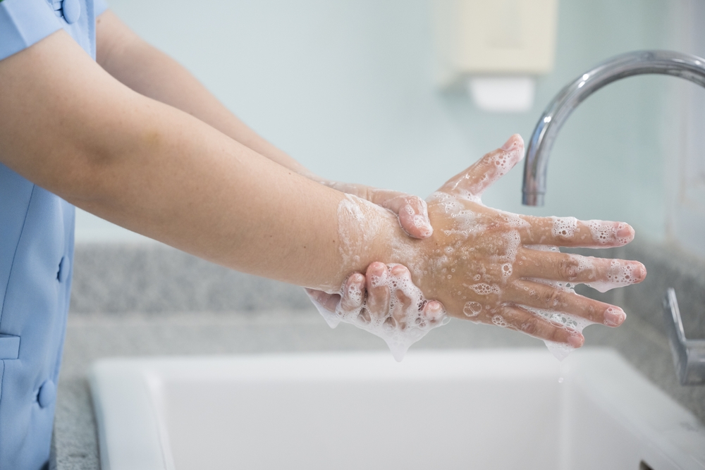 Hand washing with soap and water under sink faucet.