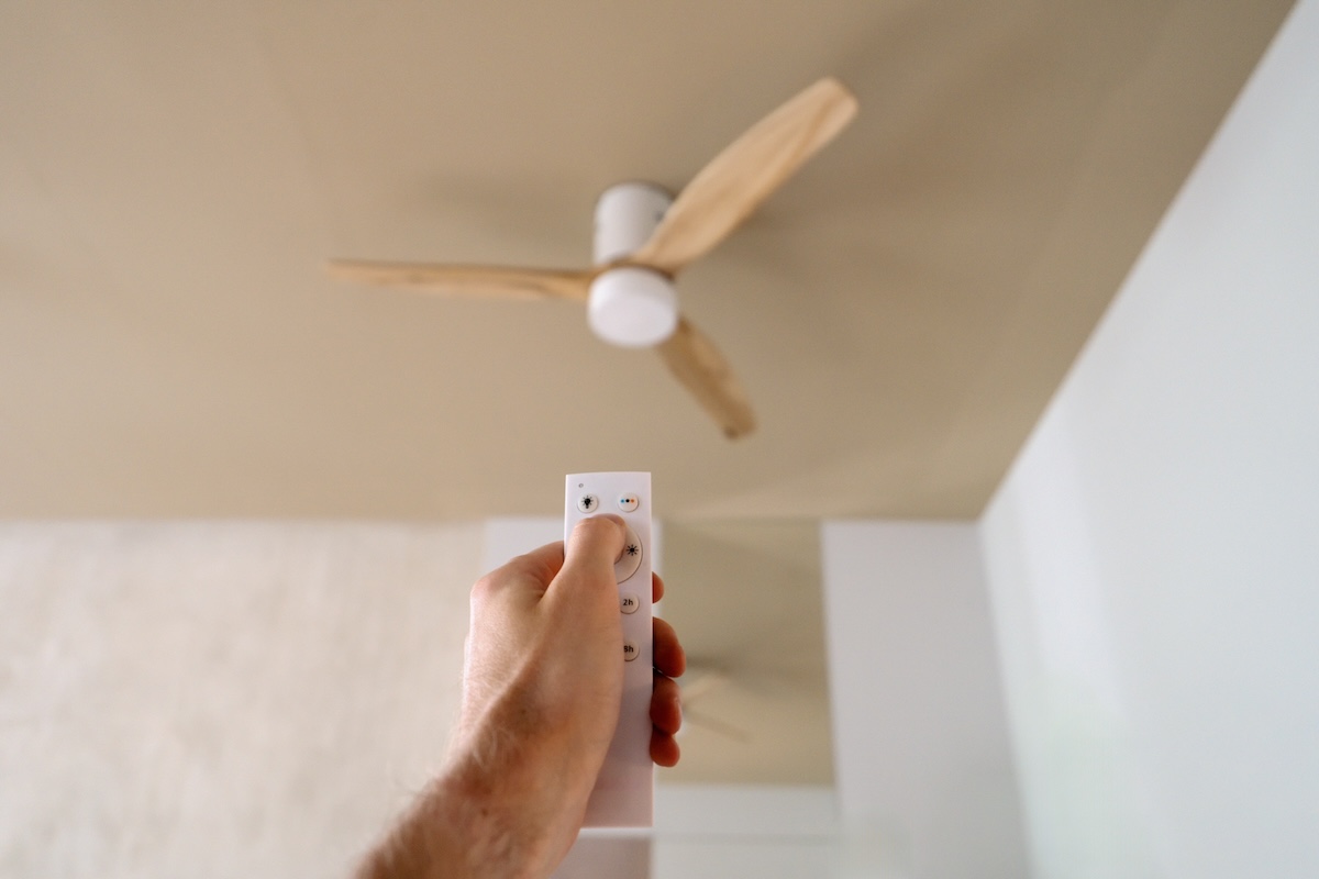 A person using a remote to change the direction of a ceiling fan during summer months.