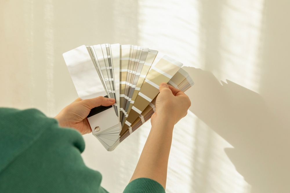 Faceless person holding a paint color swatch book of neutral colors.