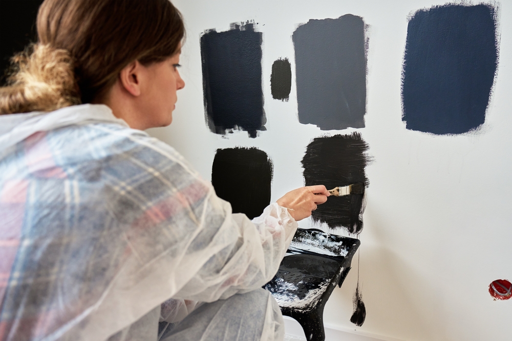 Woman painting dark paint swatches on a white wall.