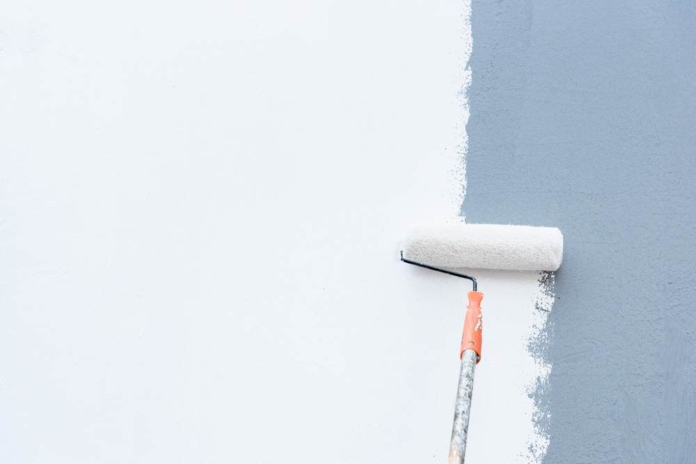 Paint roller with white paint covering up a dark gray wall.