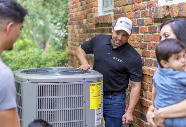 An HVAC technician installing an American Standard heat pump outside of a residential home.