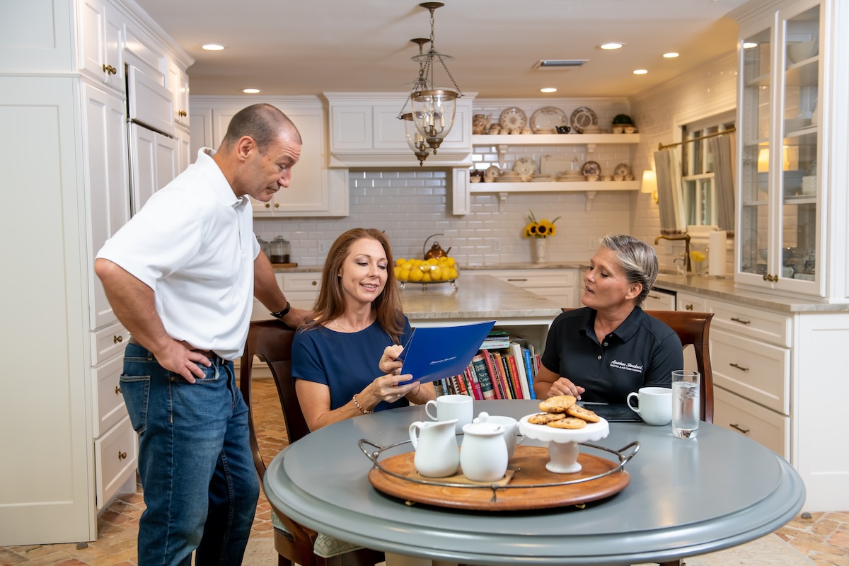 A couple sitting at a table with an American Standard technician getting ready to install a heat pump in their home.