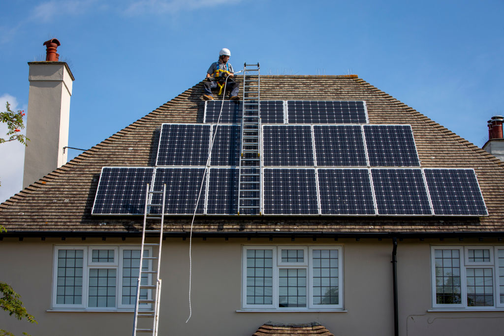 A male worker on the roof of a house installing solar panels.