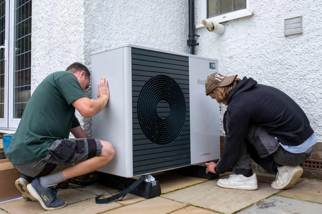 Two men installing an air source heat pump outside of a house.