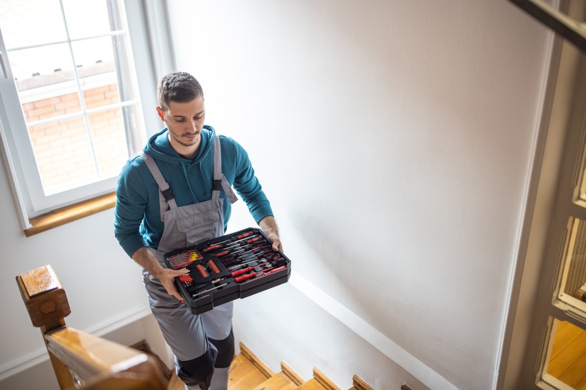 Man holding a toolbox while he climbs stairs in a house.