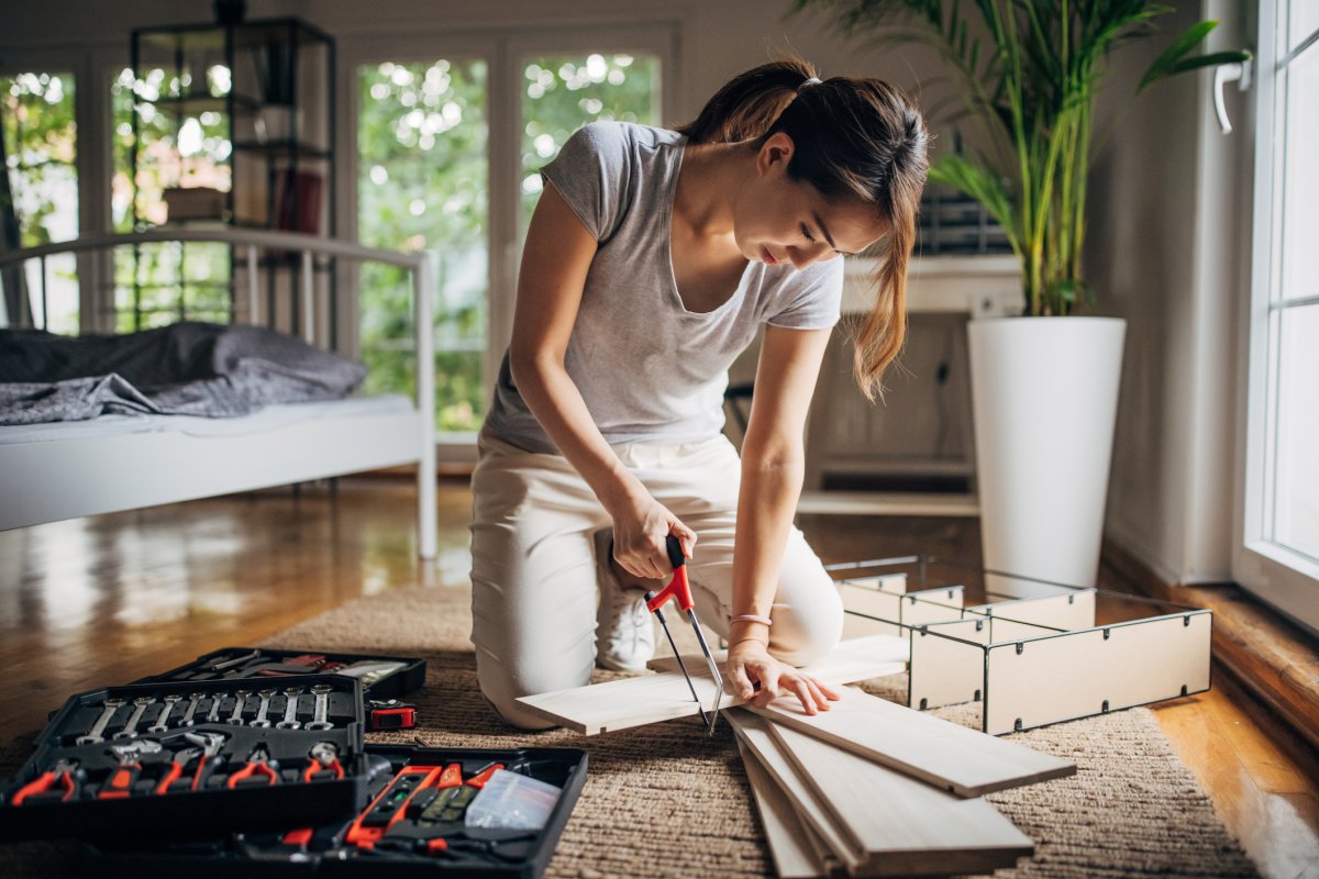 A woman assembling a shelf on the floor in bedroom at home next to tools.