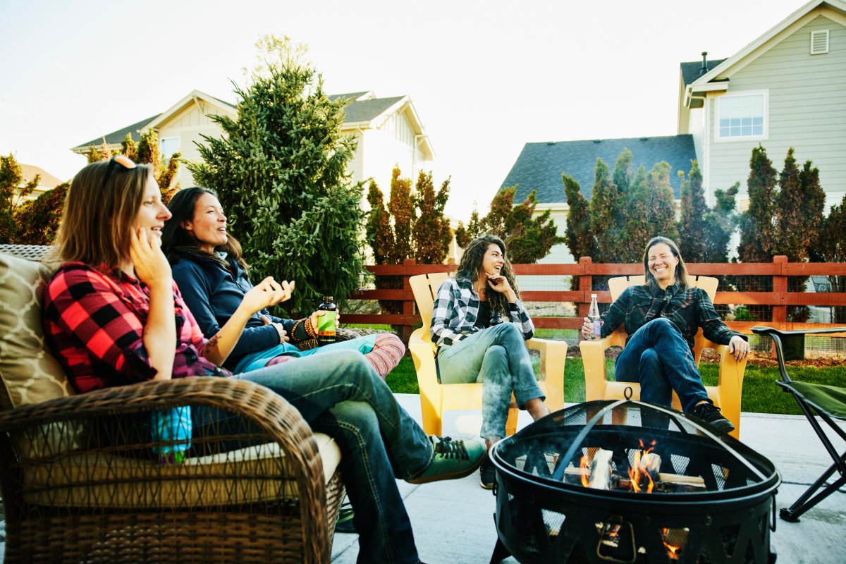 Smiling women sitting around a fire pit outside in a backyard.