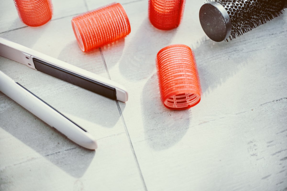 Hair flat iron and orange curlers sitting out on a bathroom countertop.