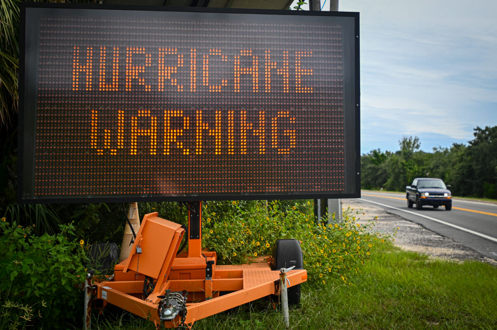 A sign displays a hurricane warning along a roadside.