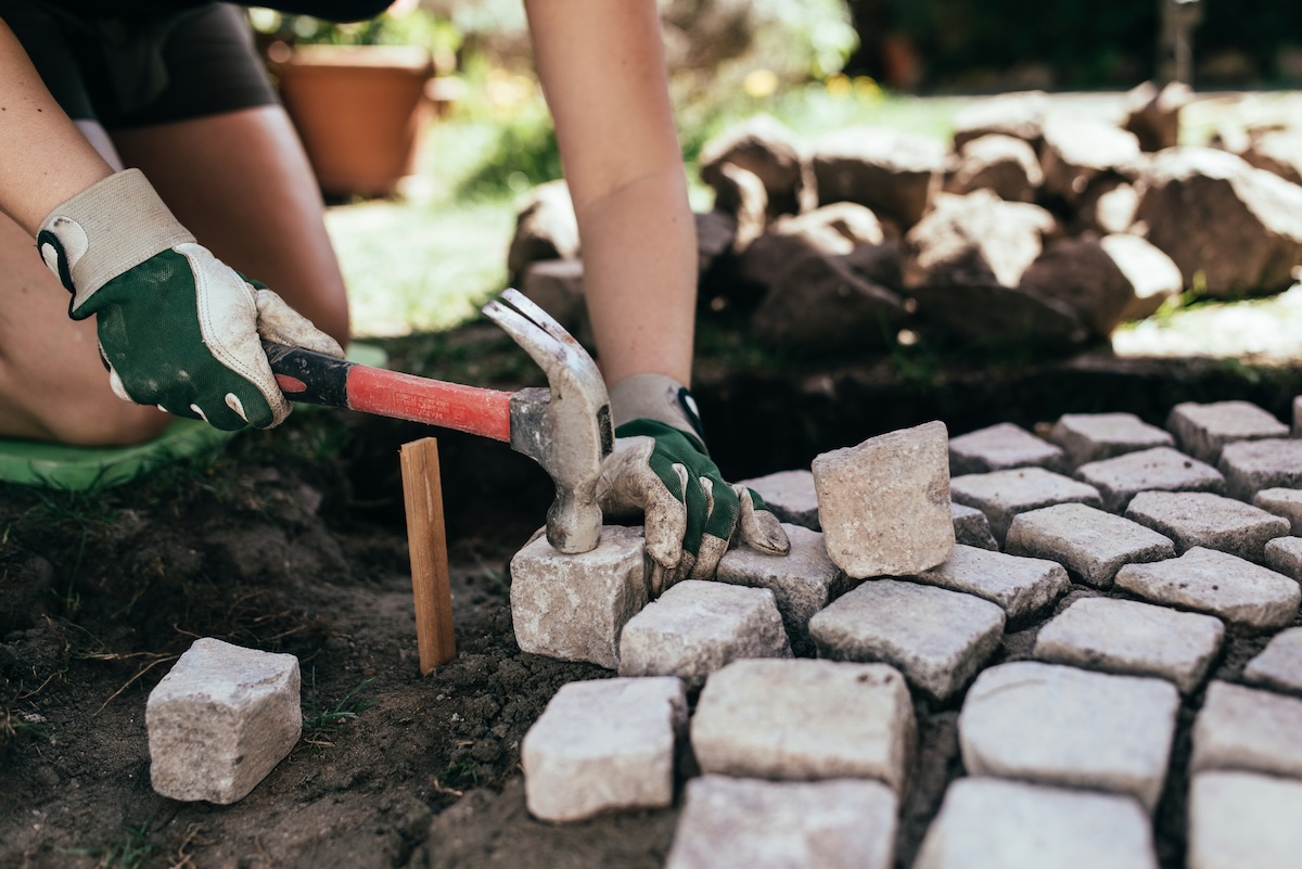 A DIYer laying small stones in the yard to make a cheap DIY garden path.