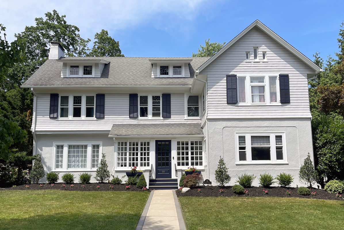 White two-story house with black shutters and white stone on the first story.