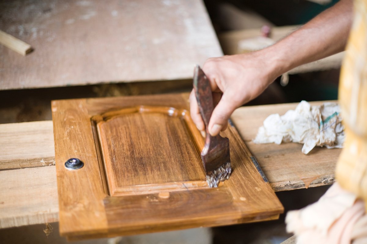Person varnishing a wooden cabinet door..