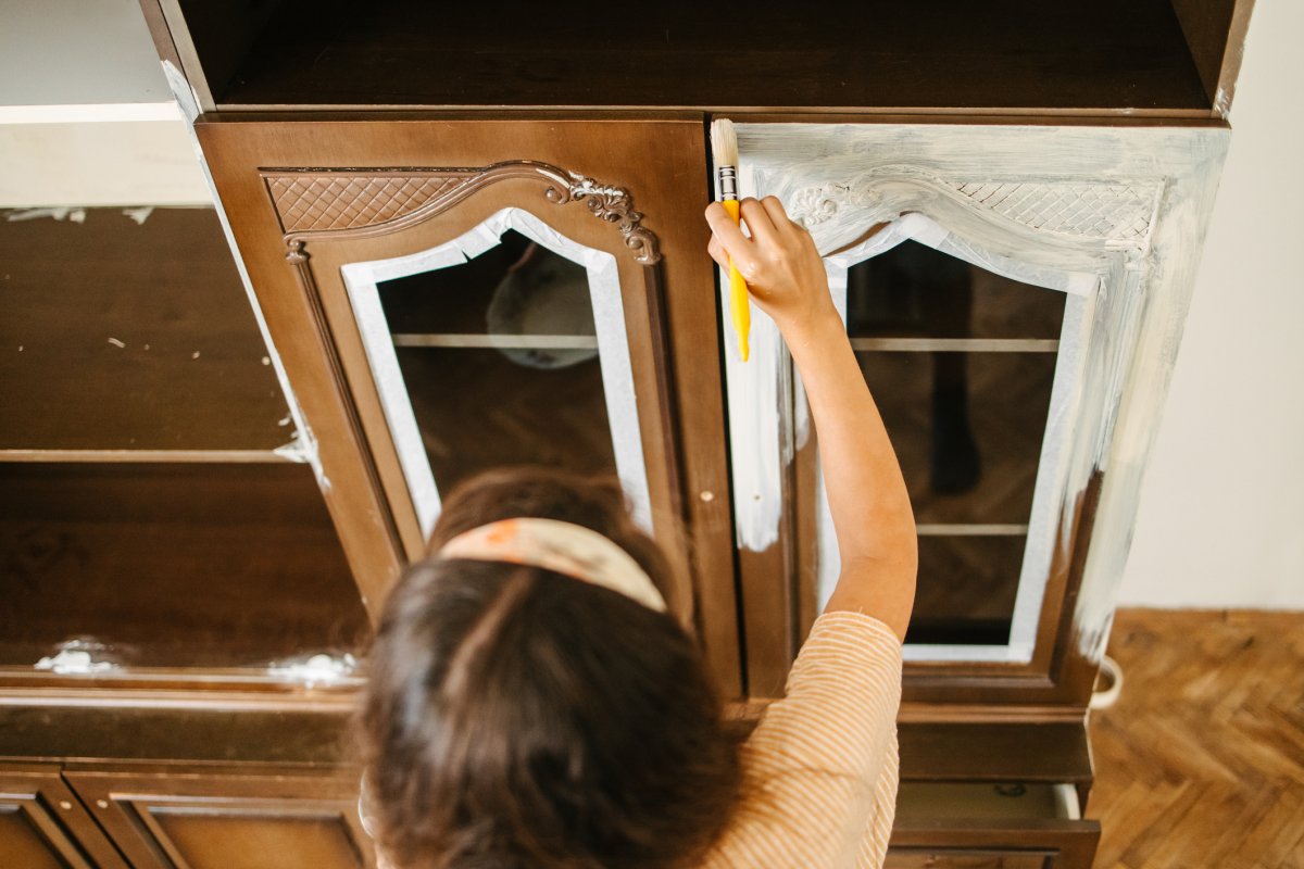 A woman painting an old china cabinet from brown to white.