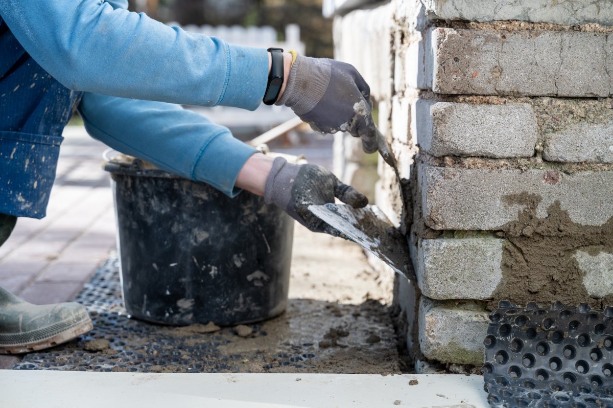 Faceless man sealing cracks in house foundation.