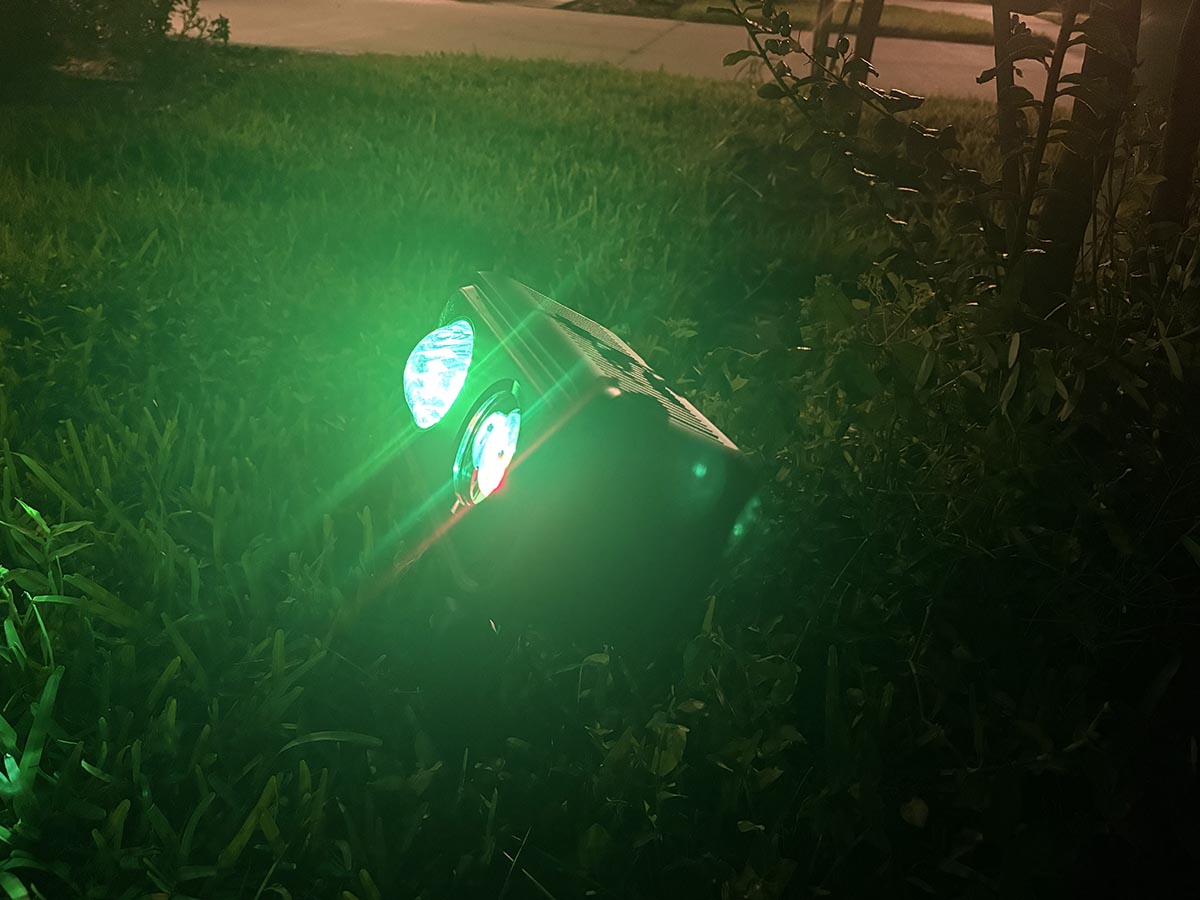Govee Christmas light projector staked in grass with green lights on