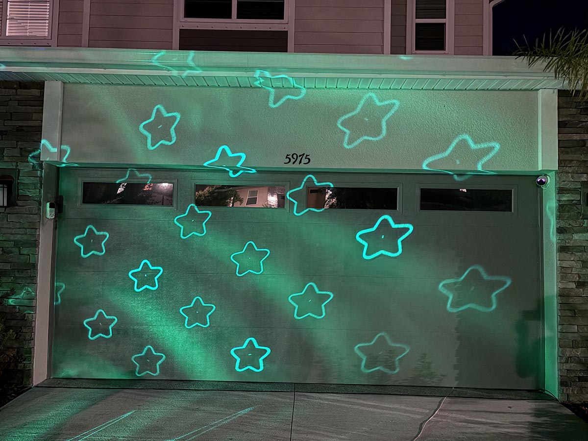 Govee Christmas light projector displaying green stars on garage door at night