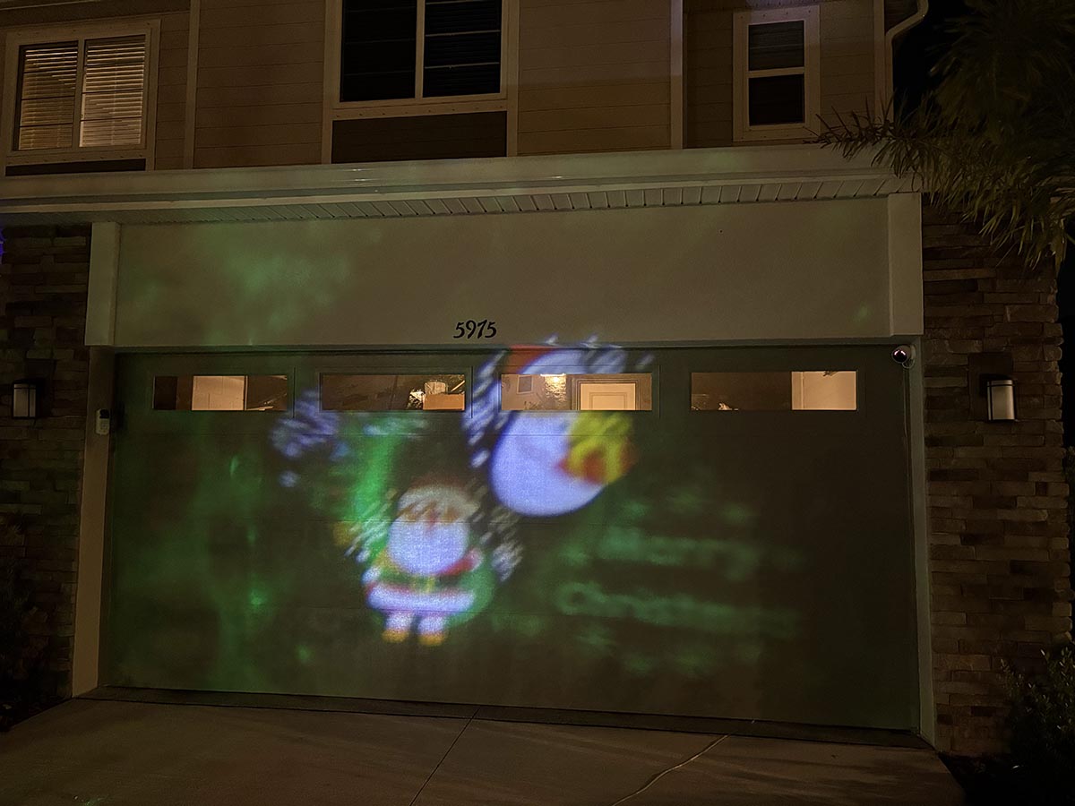Minetom Christmas light projector displaying Santas on a garage door at night
