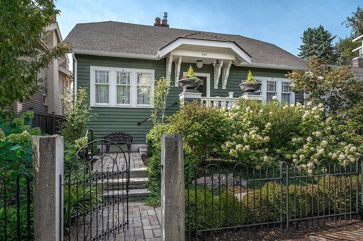 A green bungalow home with a wrought-iron front gate.