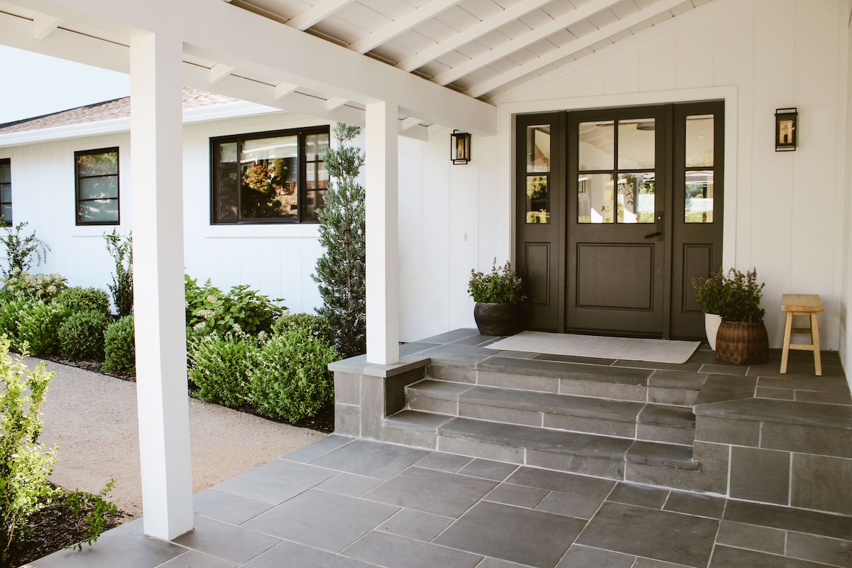 A white farmhouse home with a stoned front porch, which is covered by a wooden awning.