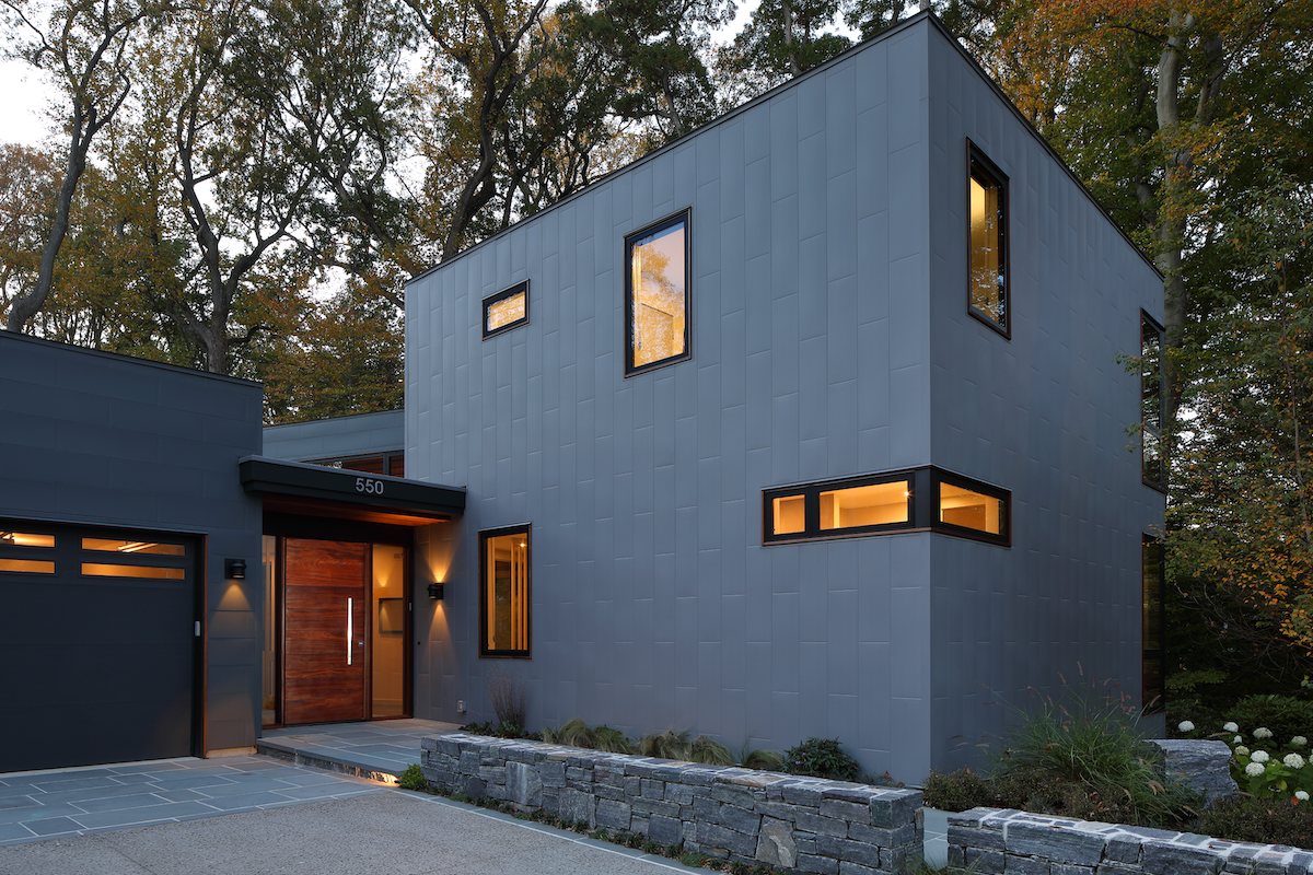 A grey modern home with lit windows and a stylish front door.