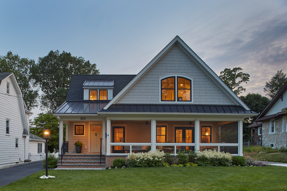 A farmhouse style home with a large, roofed porch surrounded by hydrangeas.