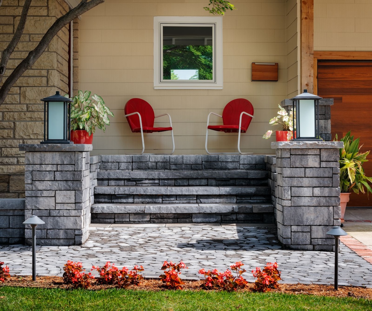 A front porch made of grey stone with red vintage chairs on its stoop.