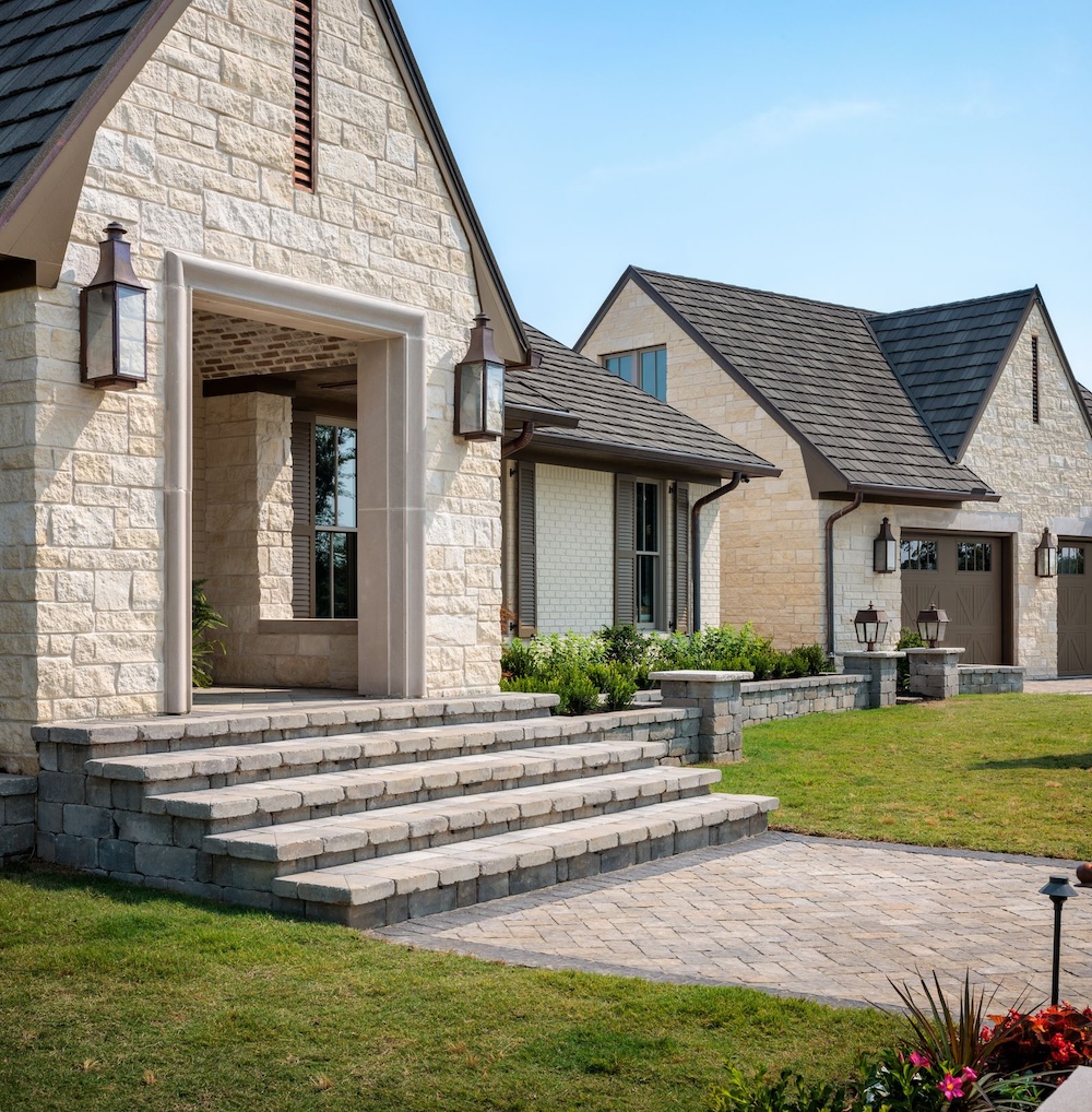 A large home with an A-shaped front porch with beige brick, lantern sconces, and a walkway.