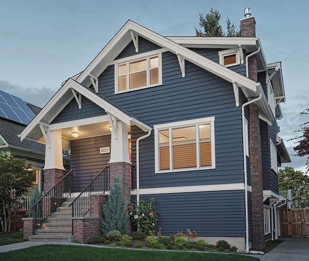 A blue craftsman bungalow with sturdy handrails and bright lights on the front stoop.
