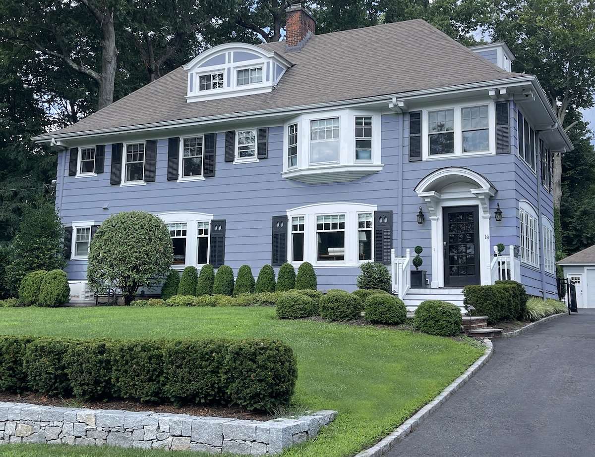 Light bluish 2-story house with a low stone wall around the front of the property.
