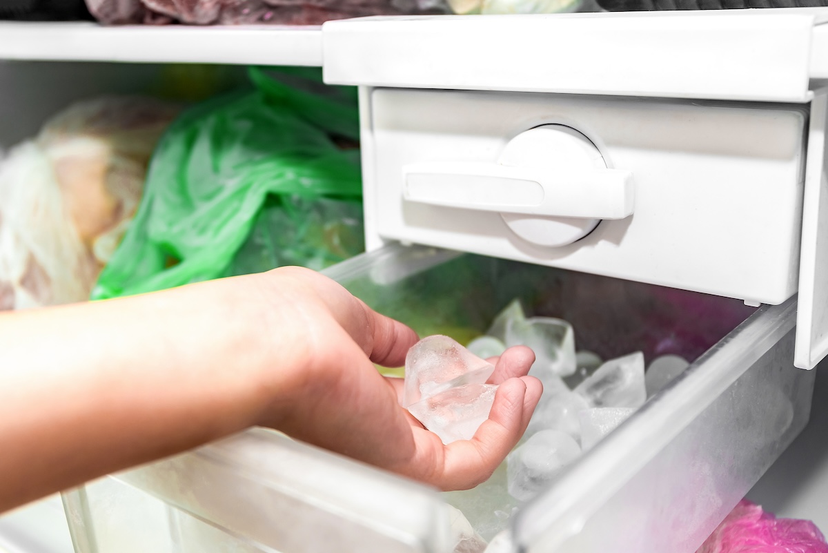 A woman's hand scoops ice from an ice maker in a freezer.