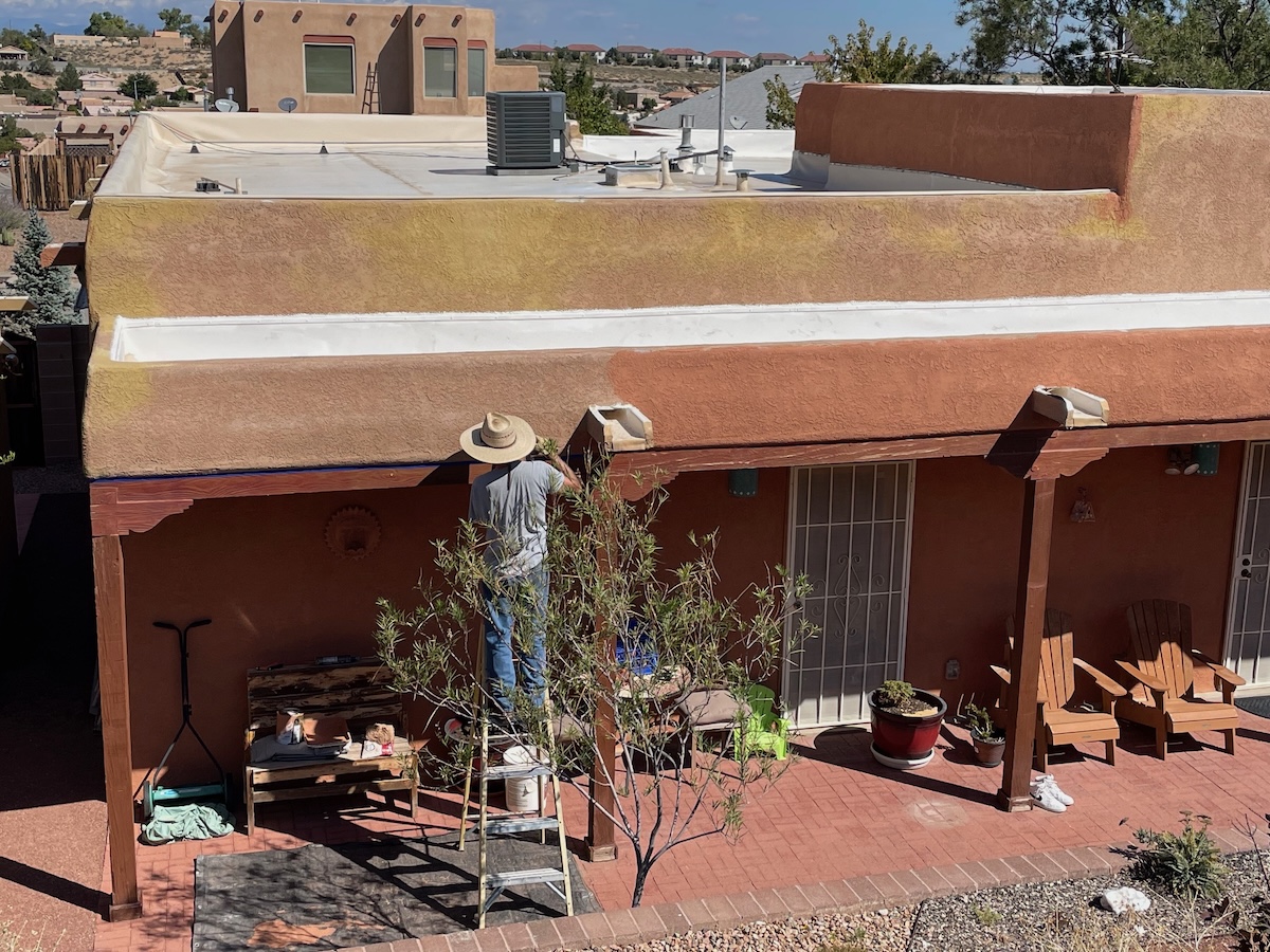 A homeowner on a ladder repainting part of a stucco house in the desert southwest.