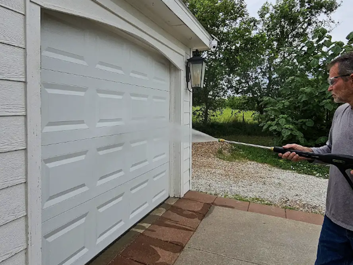 A man in a grey shirt power washes a garage door.