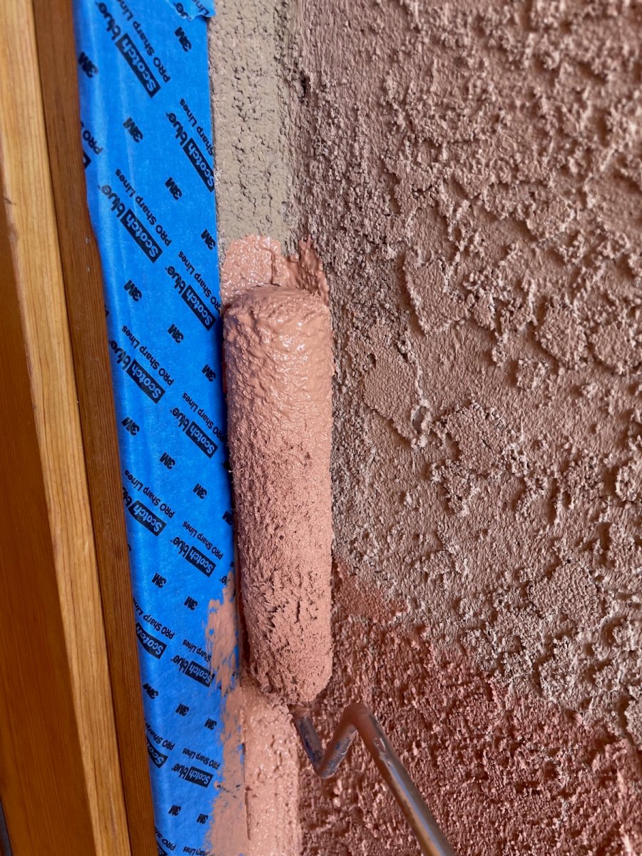 A homeowner repainting their home's stucco exterior with a mini roller and long nap cover.