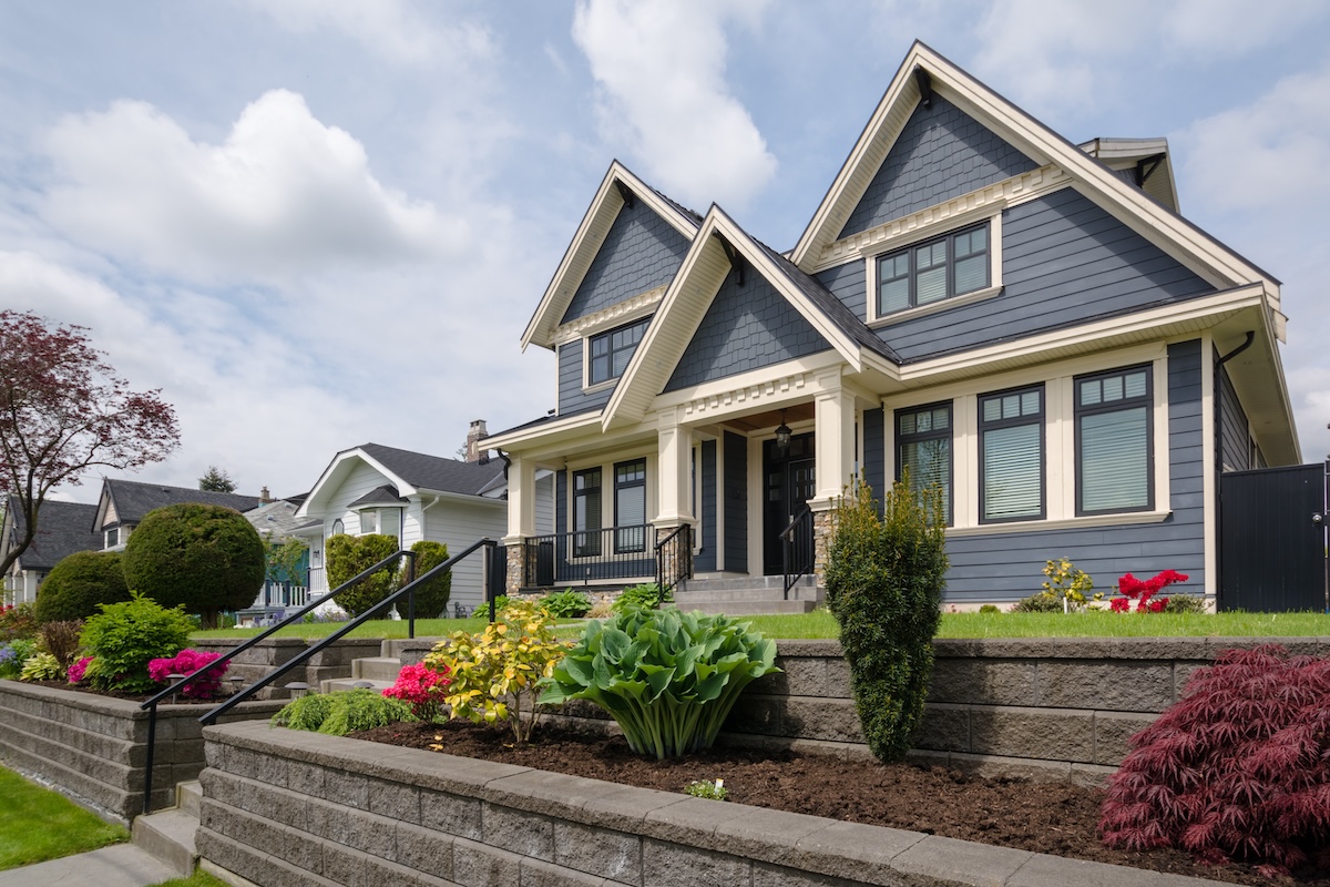 A large, beautiful home that has stairs leading from the sidewalk to the front door, complete with handrails.