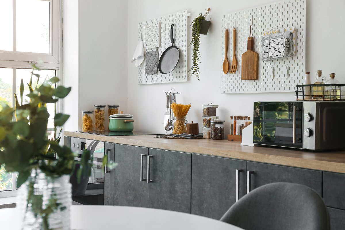 Stylish modern kitchen with utensils, pans, and other kitchen items hanging on a white pegboard.
