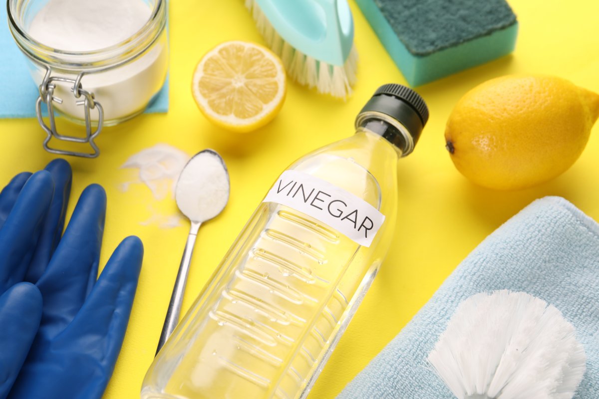 Eco friendly natural cleaners: vinegar in bottle, soda, lemons and gloves on yellow background