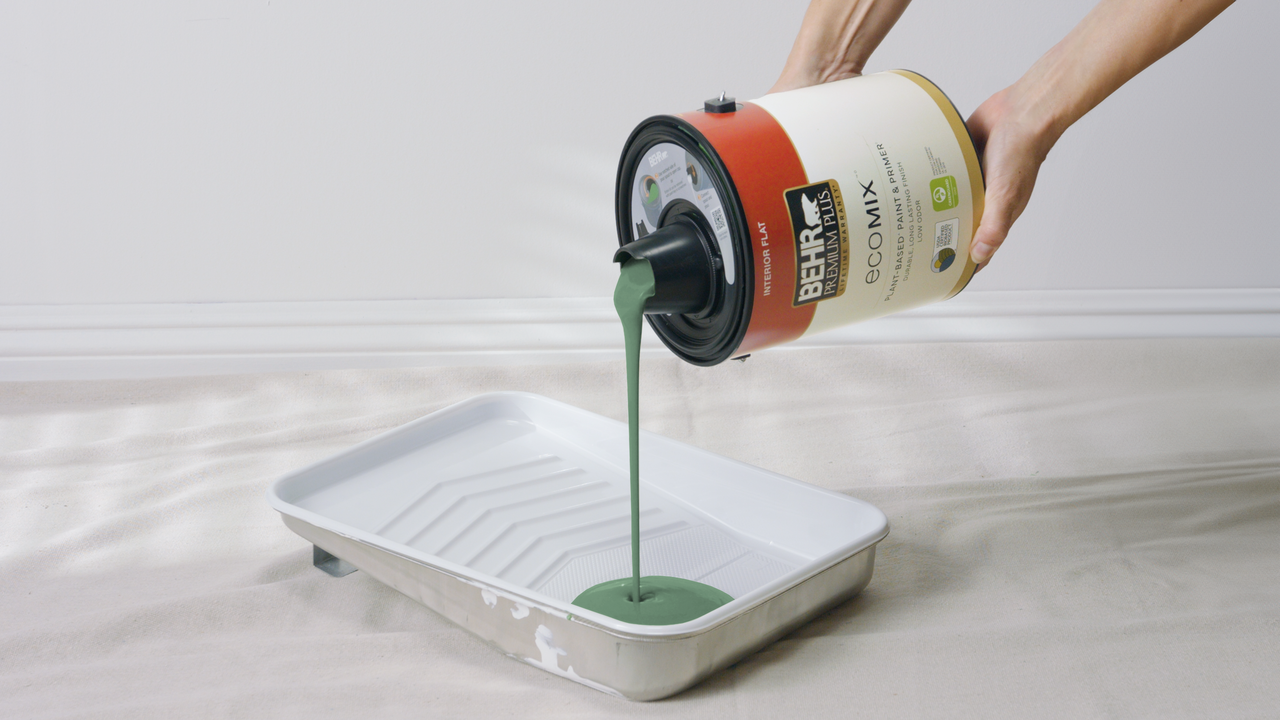 Hands pouring green Behr premium plush ecomix™ plant-based paint into a paint tray.