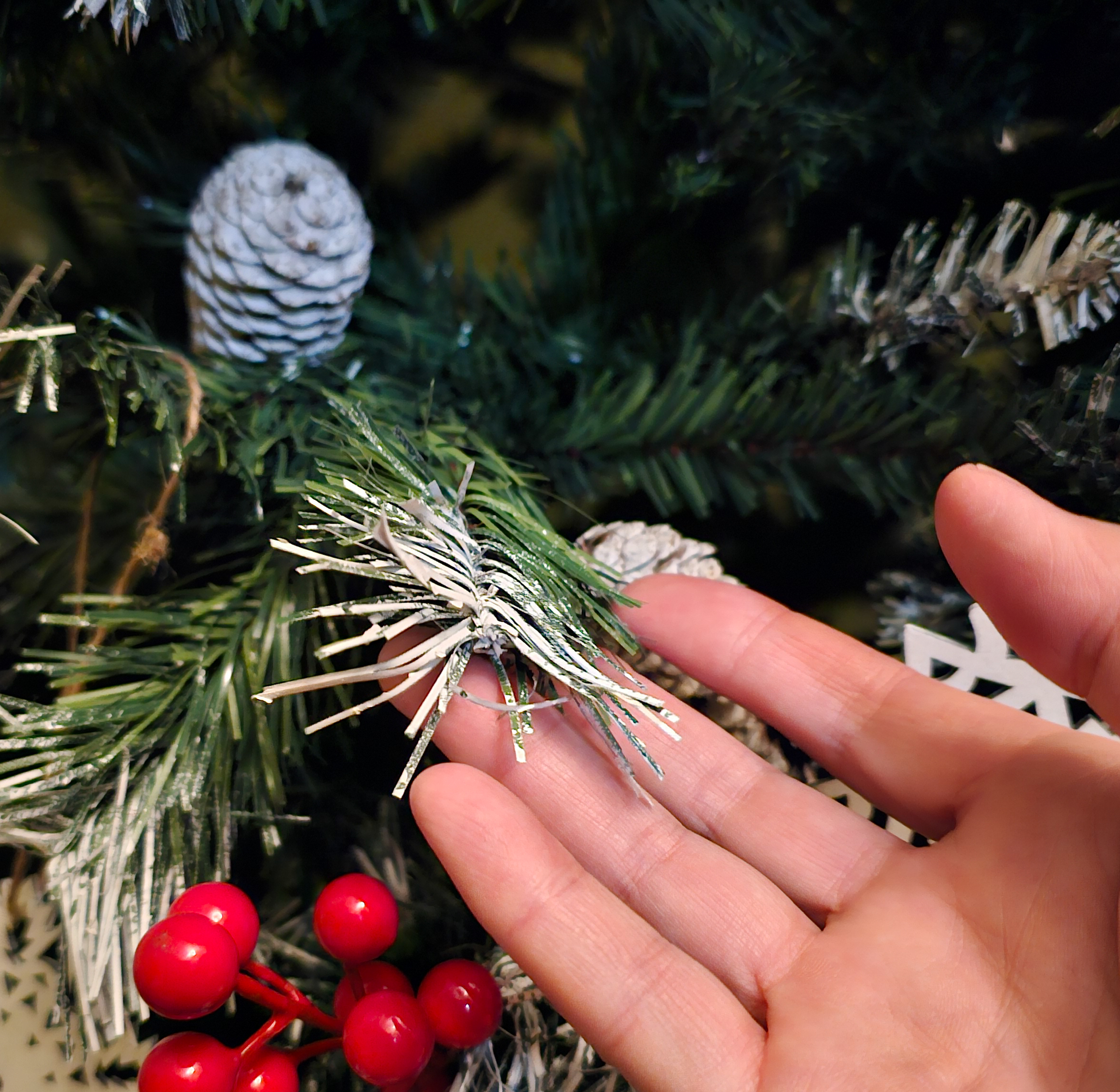 person's hand on artificial christmas tree with berries and pine cones