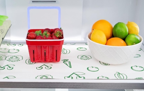 Envision refrigerator liners on a fridge shelf, with a pack of strawberries and a bowl of fruit on the shelf.