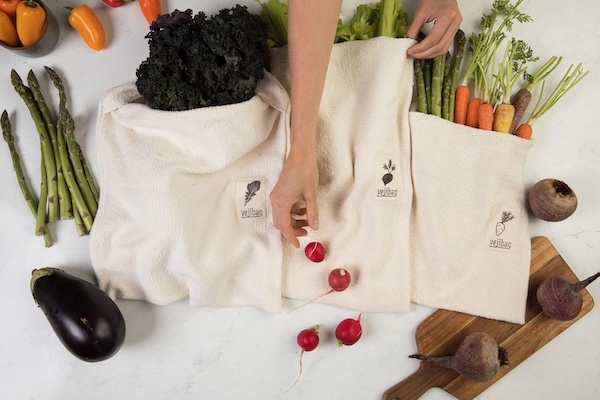 Three Vejibags with vegetables and fruits in them and scattered on a countertop.