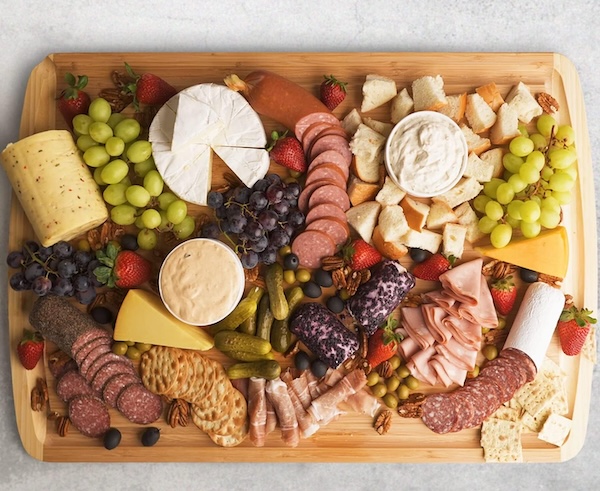 Greener Chef oversized bamboo cutting board used as a charcuterie board, covered with cheese, grapes, crackers, and meats.
