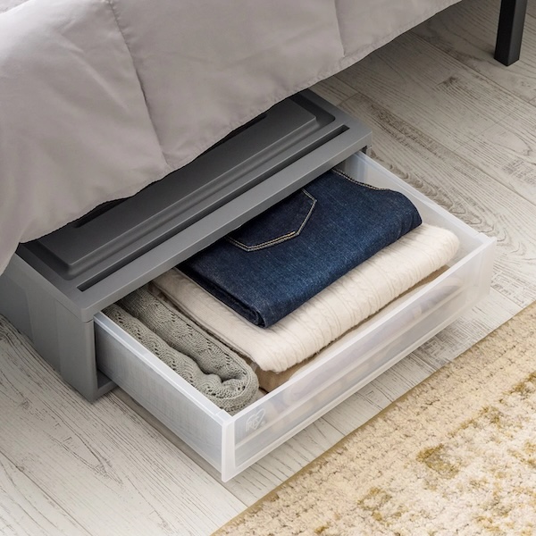 The Iris 27qt under bed drawer filled with clothes, drawer open and under a bed.