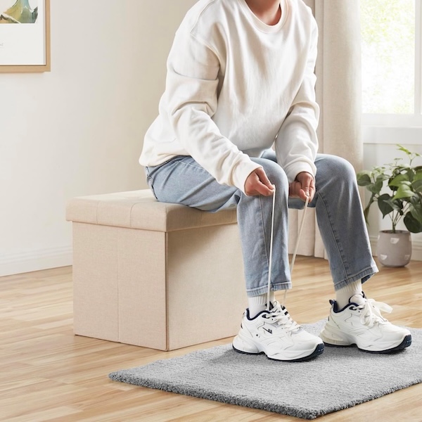 Person sitting on the Ornavo Home folding storage ottoman, tying their shoes.