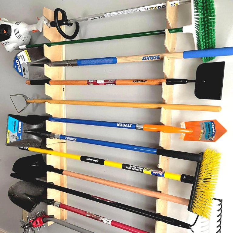 Garage tool rack made of wood filled with shovels, rakes and other yard tools.