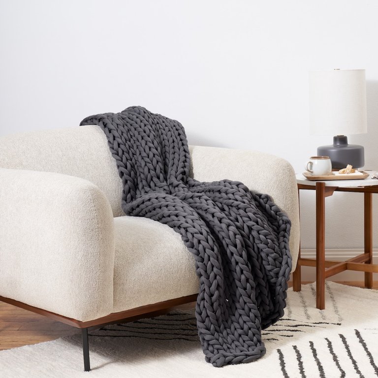 Bearaby Couch Napper blanket in dark grey over a beige chair in a minimalist living room.